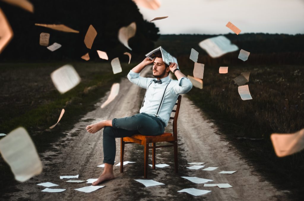 barefoot man in chair outside raining paper